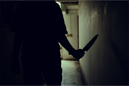 Silhouette of a person holding knife in dark hallway