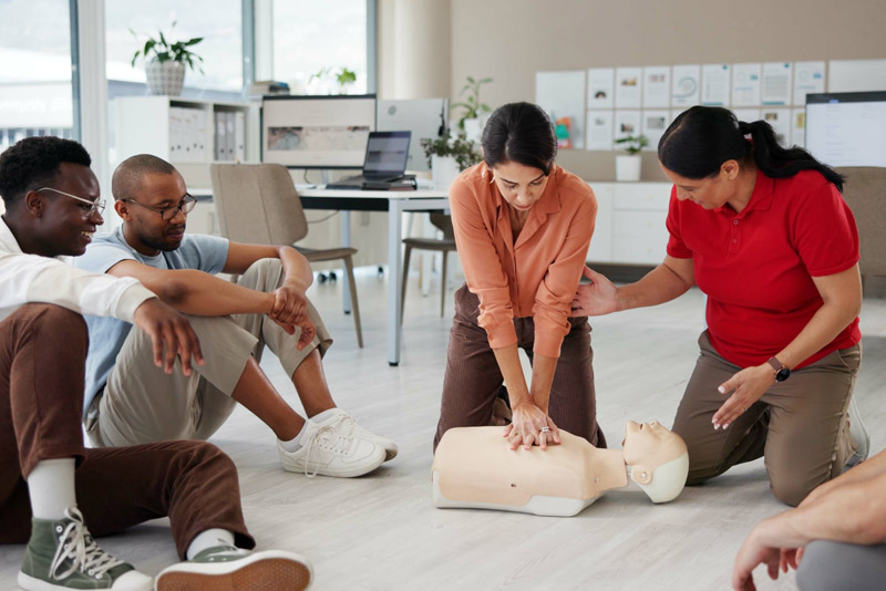 Instructor teaching a group of students and educators first aid and CPR techniques during practical workplace training.